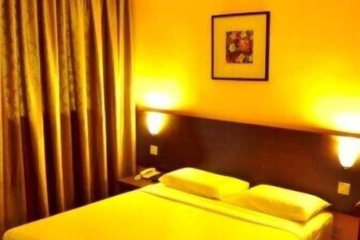 A hotel room with a large bed, two bedside lamps, a telephone, and a framed picture on the wall.