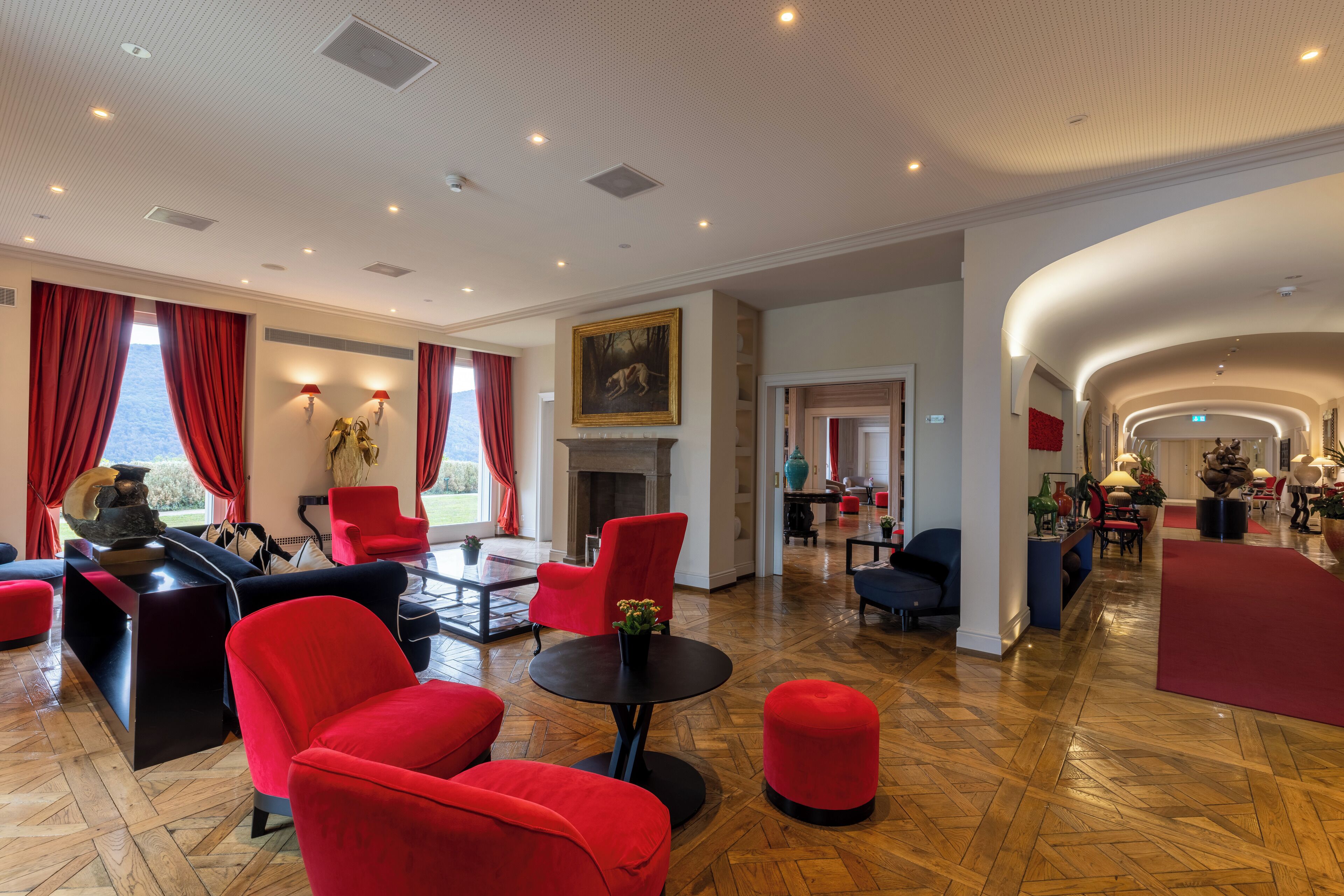 A spacious lobby with red and black upholstered seating, a fireplace, and a large painting on the wall.