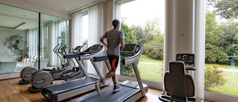 A modern gym with treadmills, a rowing machine, and a large window offering a view of the outdoors.