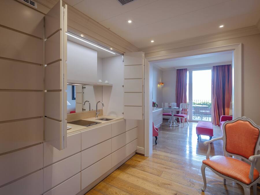 A modern kitchen with integrated appliances, a dining area with a table and chairs, and a balcony with curtains.
