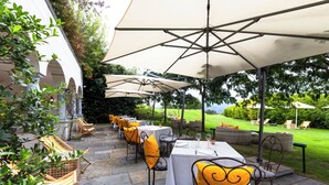 Un espacio de comedor al aire libre con mesas y sillas, sombrillas y vistas al paisaje.