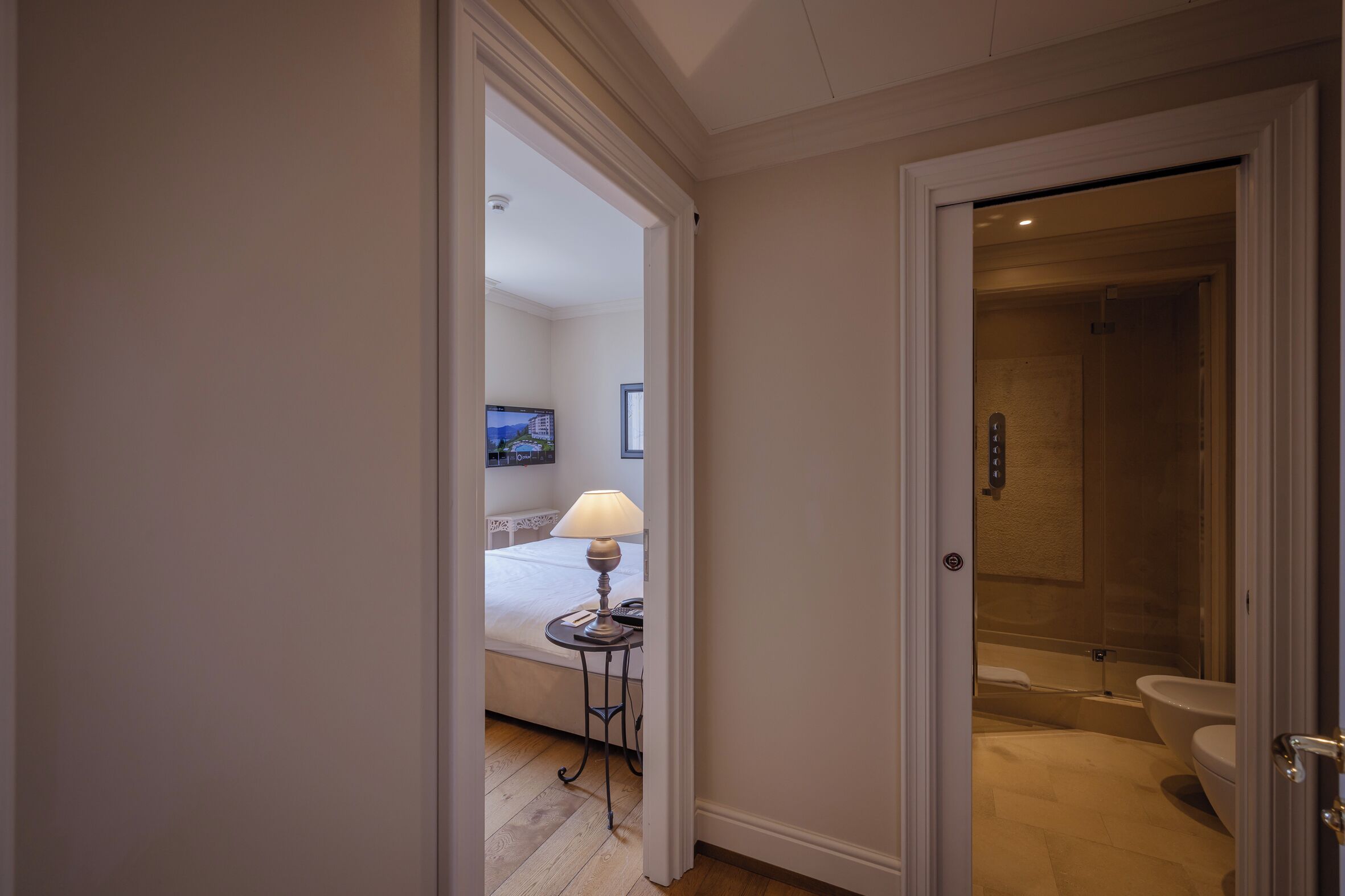 A hotel room with a bed, a bedside table with a lamp, a television, and a bathroom with a bathtub and toilet.