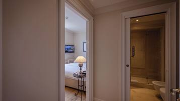 A hotel room with a bed, a bedside table with a lamp, a television, and a bathroom with a bathtub and toilet.