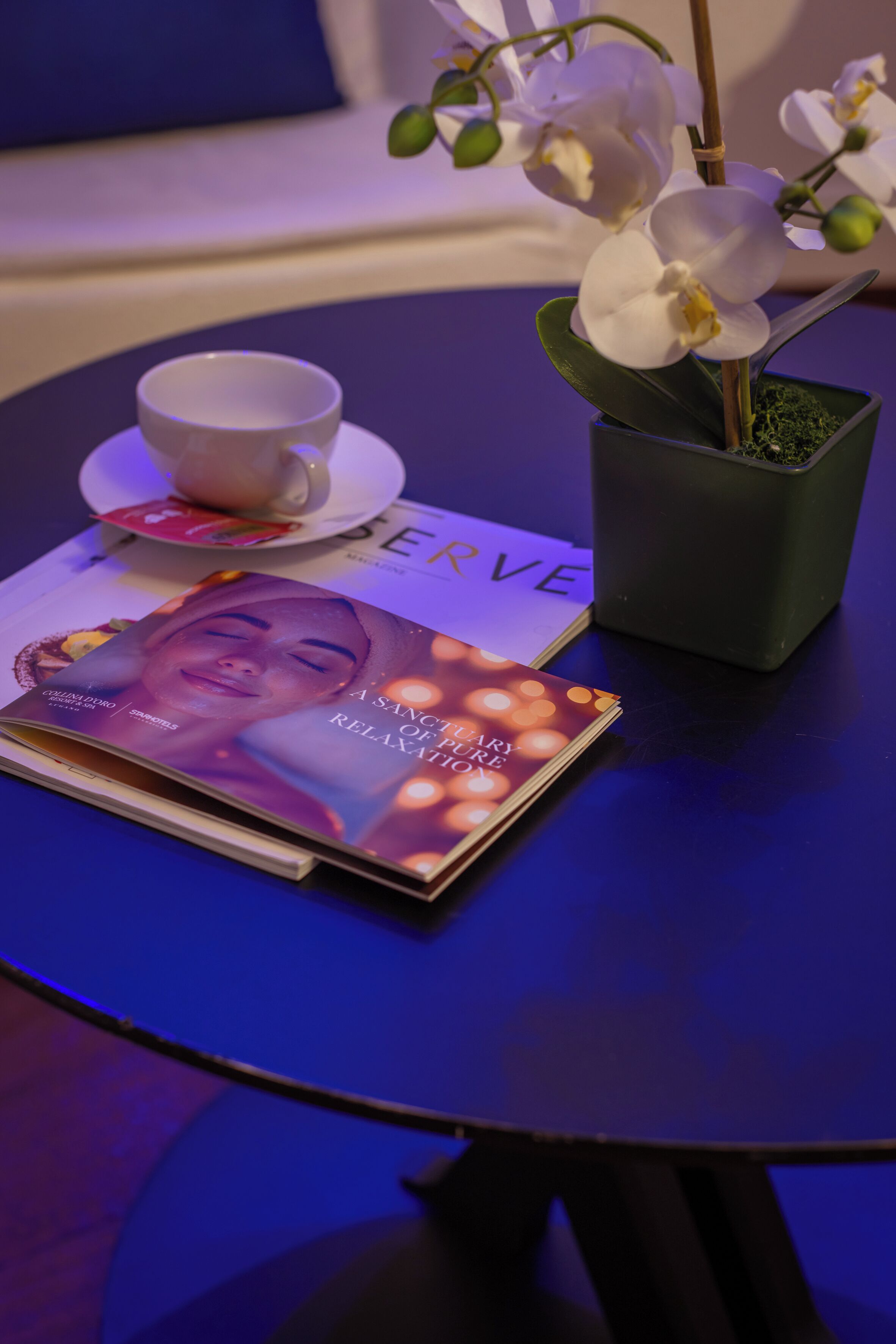 Une table avec une orchidée blanche, une tasse, une soucoupe et un magazine.