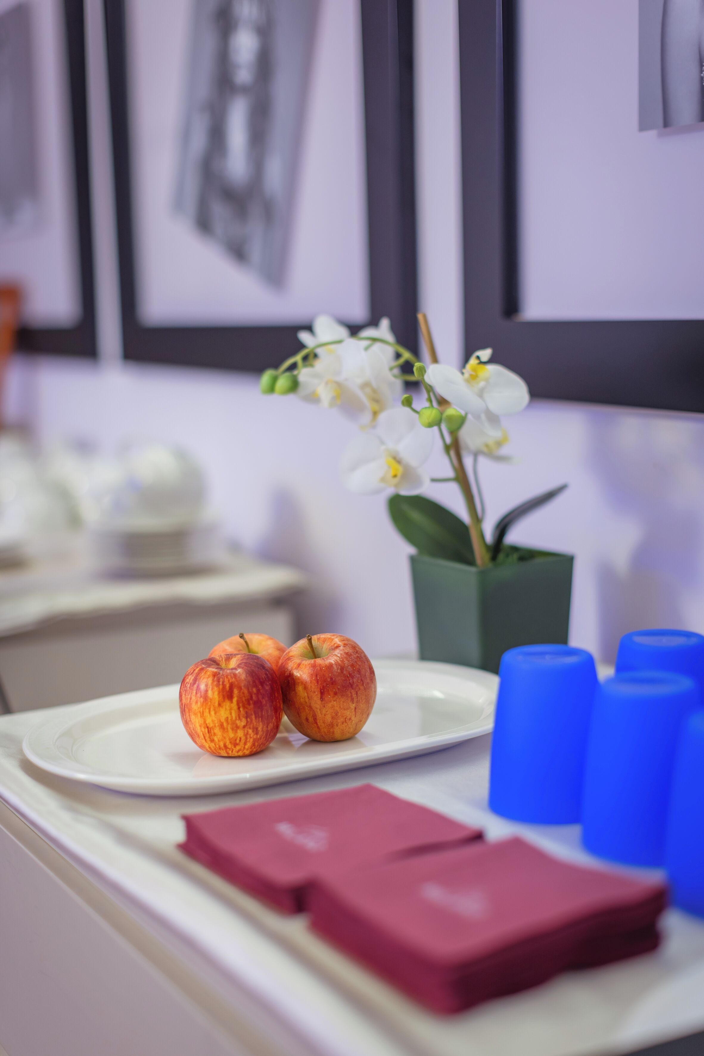 Een tafel met twee appels, een vaas met witte bloemen en blauwe bekers.