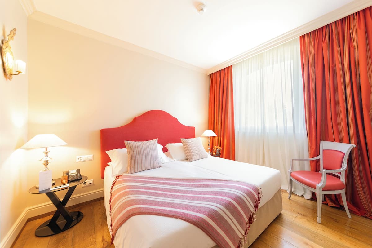 A hotel room with a bed, a chair, a nightstand, and a lamp.