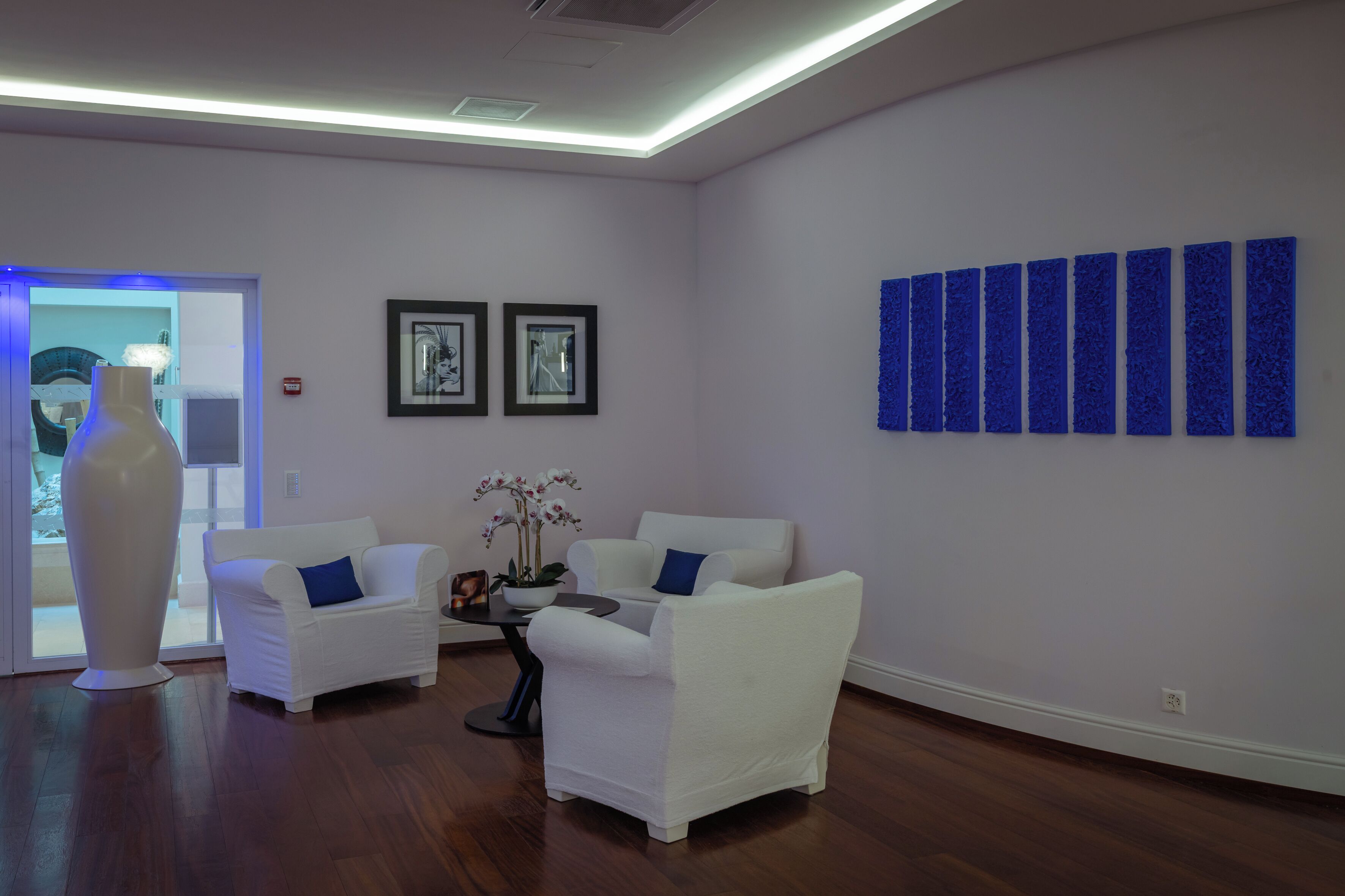 Uma sala de estar moderna com móveis brancos, uma mesa de centro e uma parede azul decorativa.