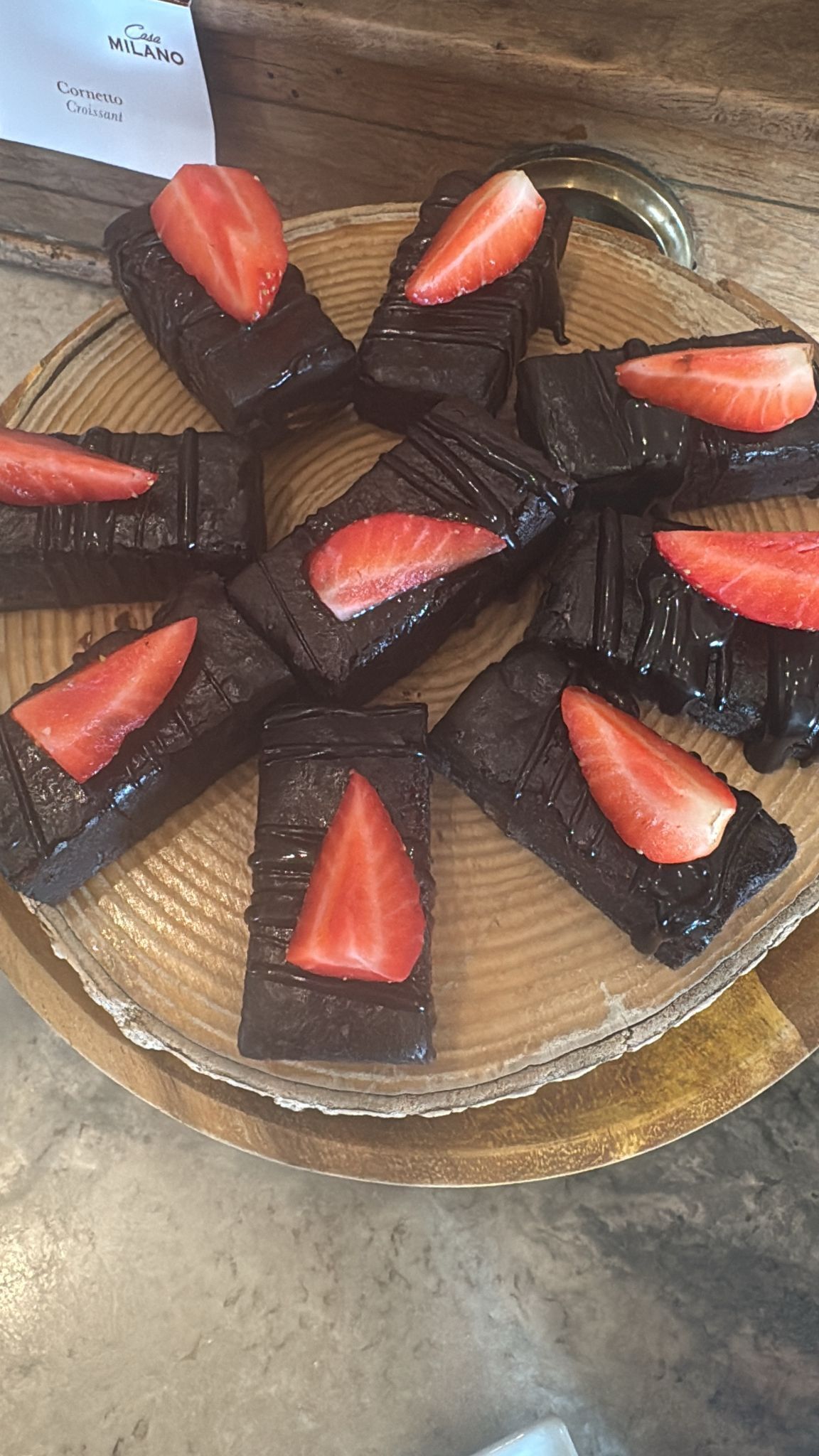 A plate of chocolate-covered desserts with strawberries on a wooden board.