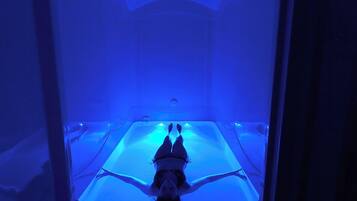 Una persona recostada en un espacio iluminado en azul con techo de vidrio, evocando un ambiente de spa o relajación.