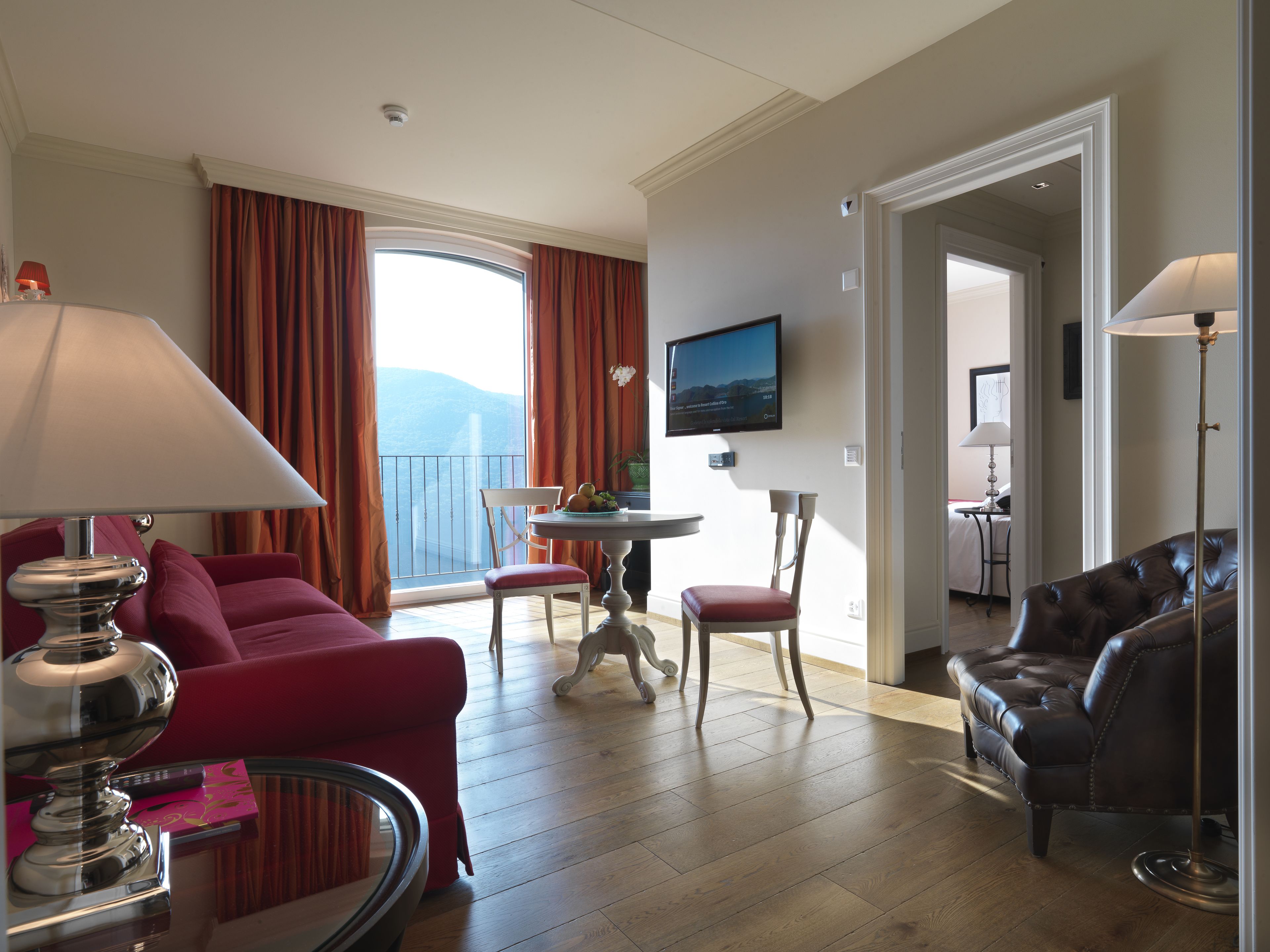 Habitació d'hotel amb balcó, televisió, taula de menjador i sofà de cuir.