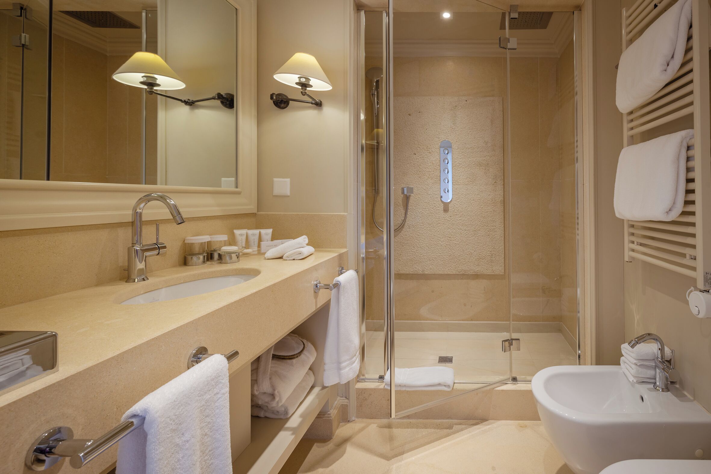 A bathroom with two sinks, a mirror, a shower, and a bidet.