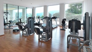 Un gimnasio amplio con diversas máquinas de ejercicio, ventanas grandes que ofrecen vistas al exterior y suelo de madera.
