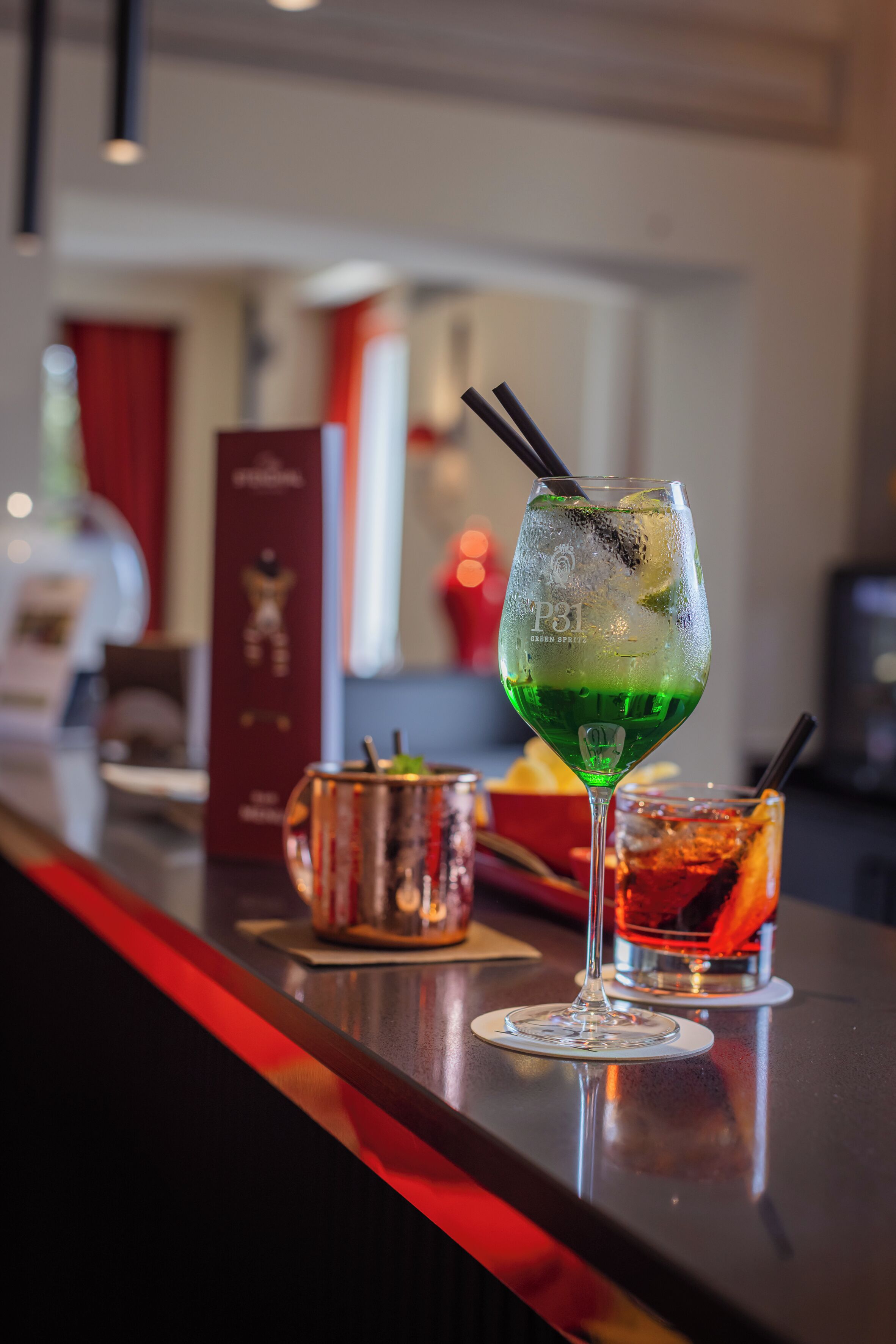 Un área de bar con un vaso de cóctel verde, una bebida roja y un atril para el menú.