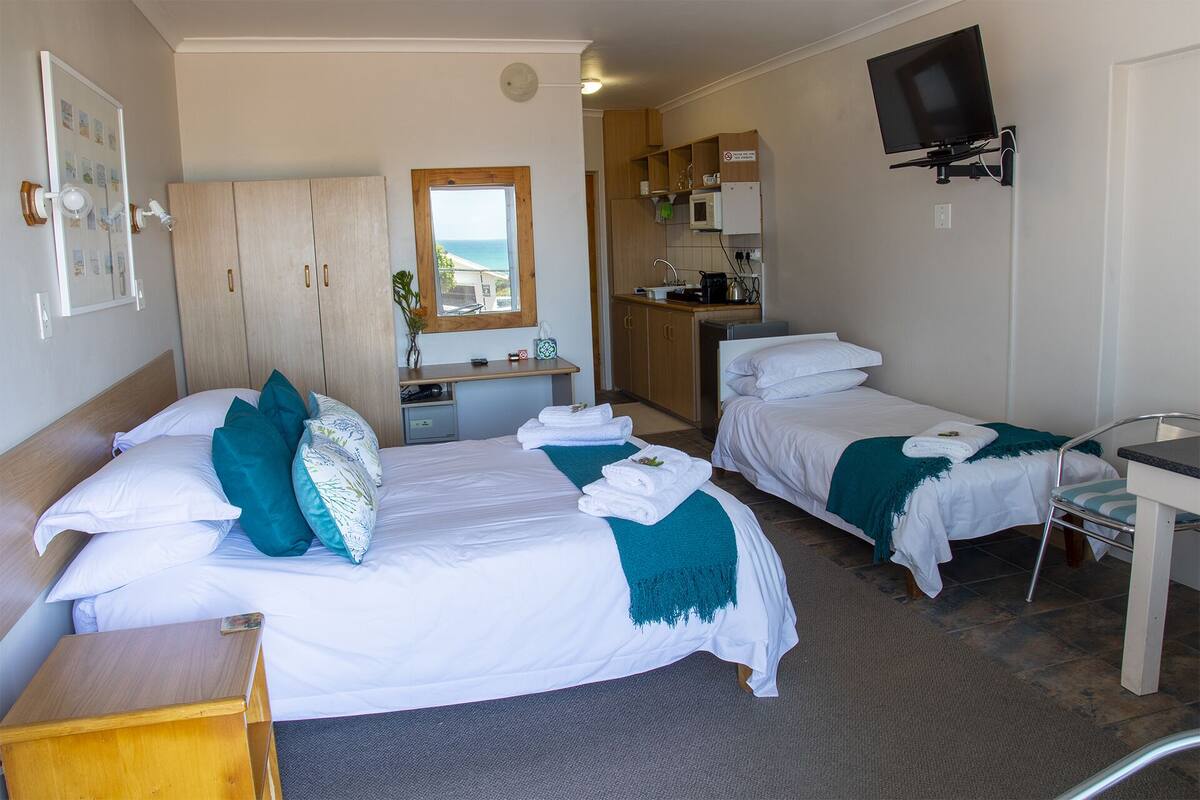 A hotel room with two beds, a desk, a kitchenette, and a TV.