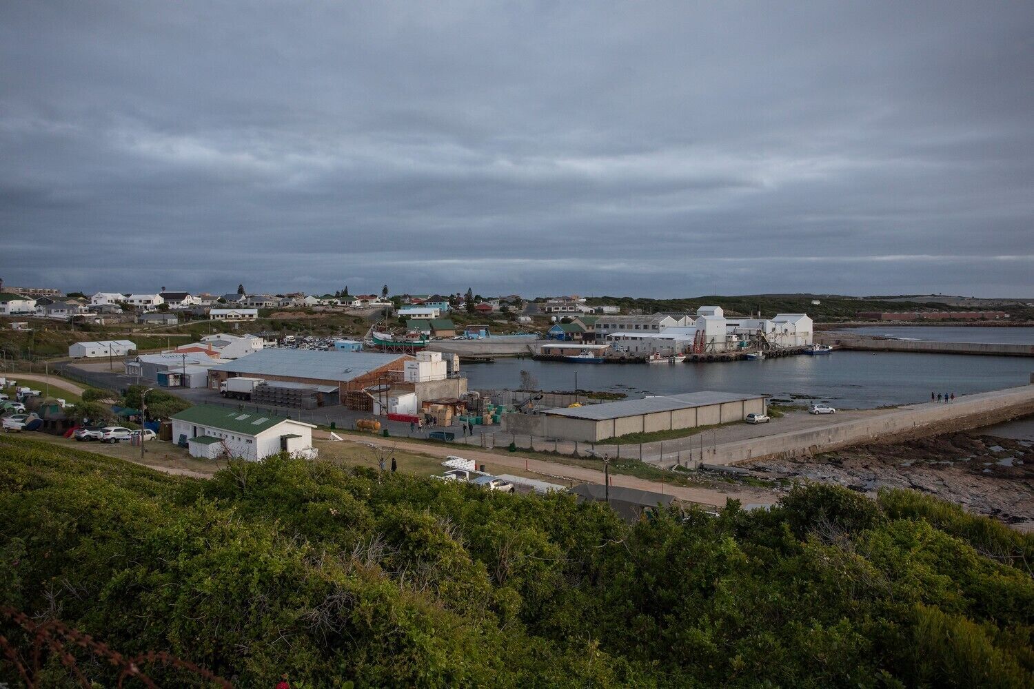A coastal industrial area with warehouses, a dock, and a road leading to a residential area.