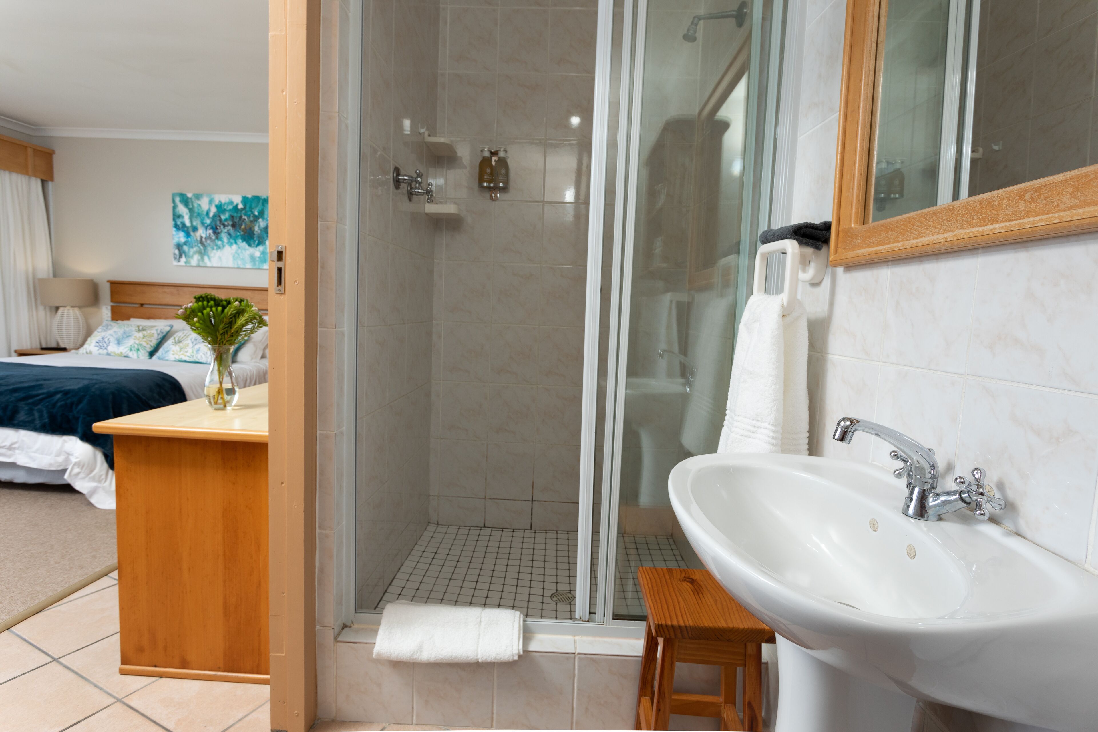 A hotel bathroom with a shower, sink, and a wooden stool.