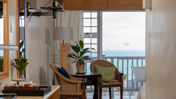A room with a view of the ocean, a wicker chair, a table with a lamp, and a potted plant. - Aire del Mar Guest House (Kleinbaai)