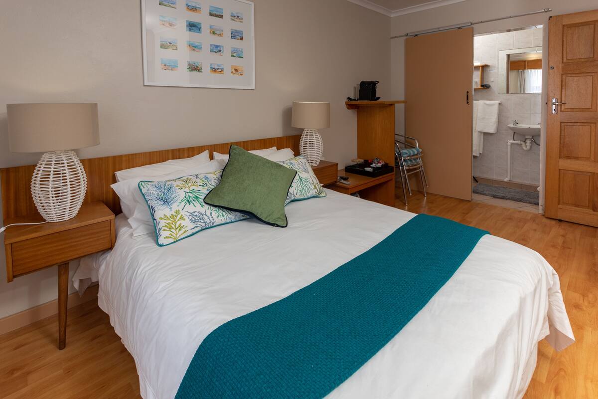 A neatly made bed with a teal throw, two bedside lamps, and a framed picture on the wall.