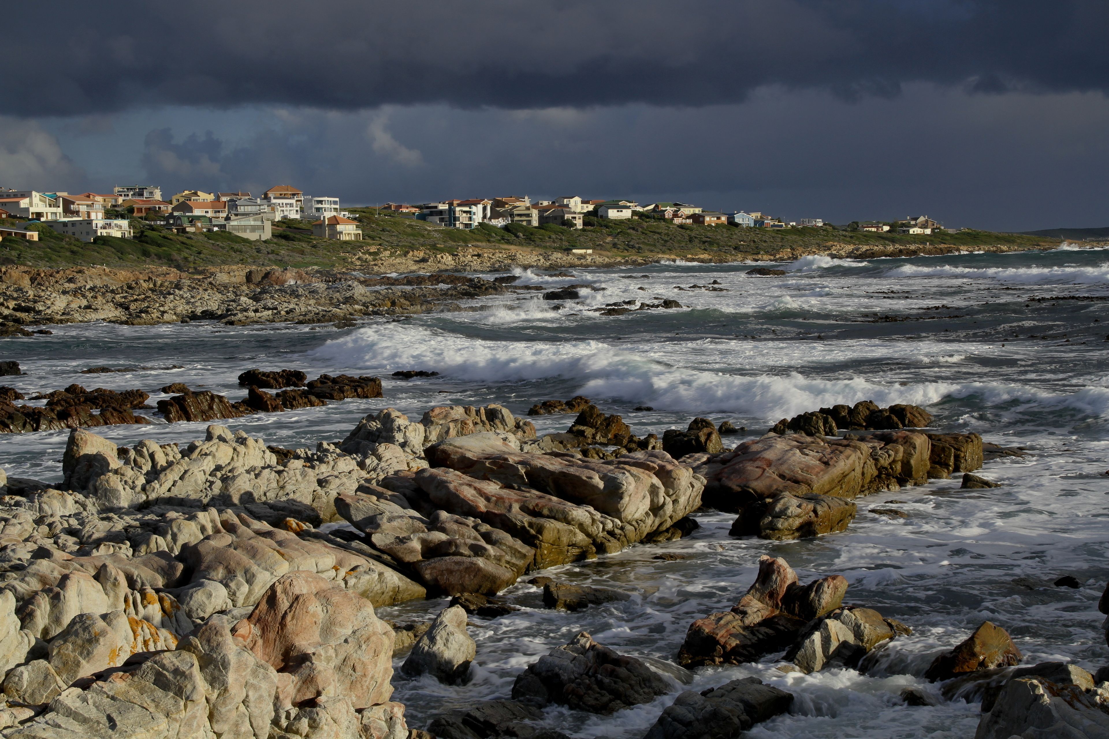 A coastal area with rocky terrain and buildings in the background.