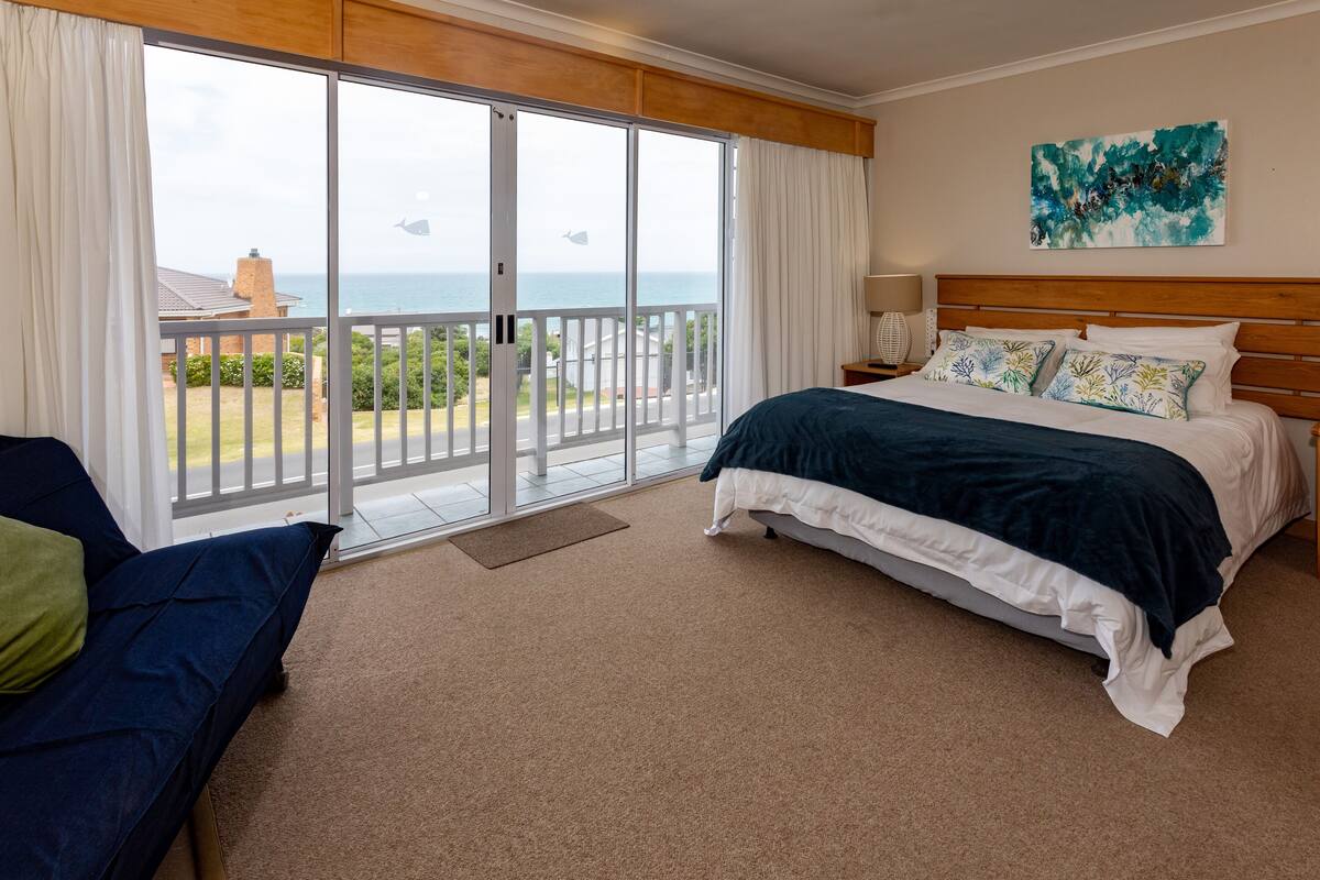A bedroom with a large sliding glass door leading to a balcony with a view of the sea.
