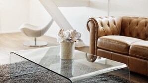 En moderne stue med et glasbord, en lædersofa i brunt skind og en vase med blomster.