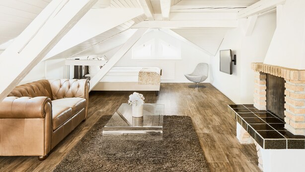 Et rum på loftet med en lædersofa, et glastæppe, en pejs og en moderne stol.