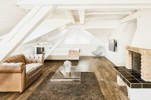 An attic room with a leather sofa, a glass coffee table, a fireplace, and a modern chair. - Hotel Schäfli (Uzwil)