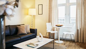 En moderne stue med en sort lædersofa, et hvidt sofabord med en bog, en hvid stol og et spisebord med frugt.