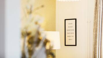 Una habitación con una lámpara fijada a la pared, una cita inspiradora enmarcada y una planta decorativa a medio ver.