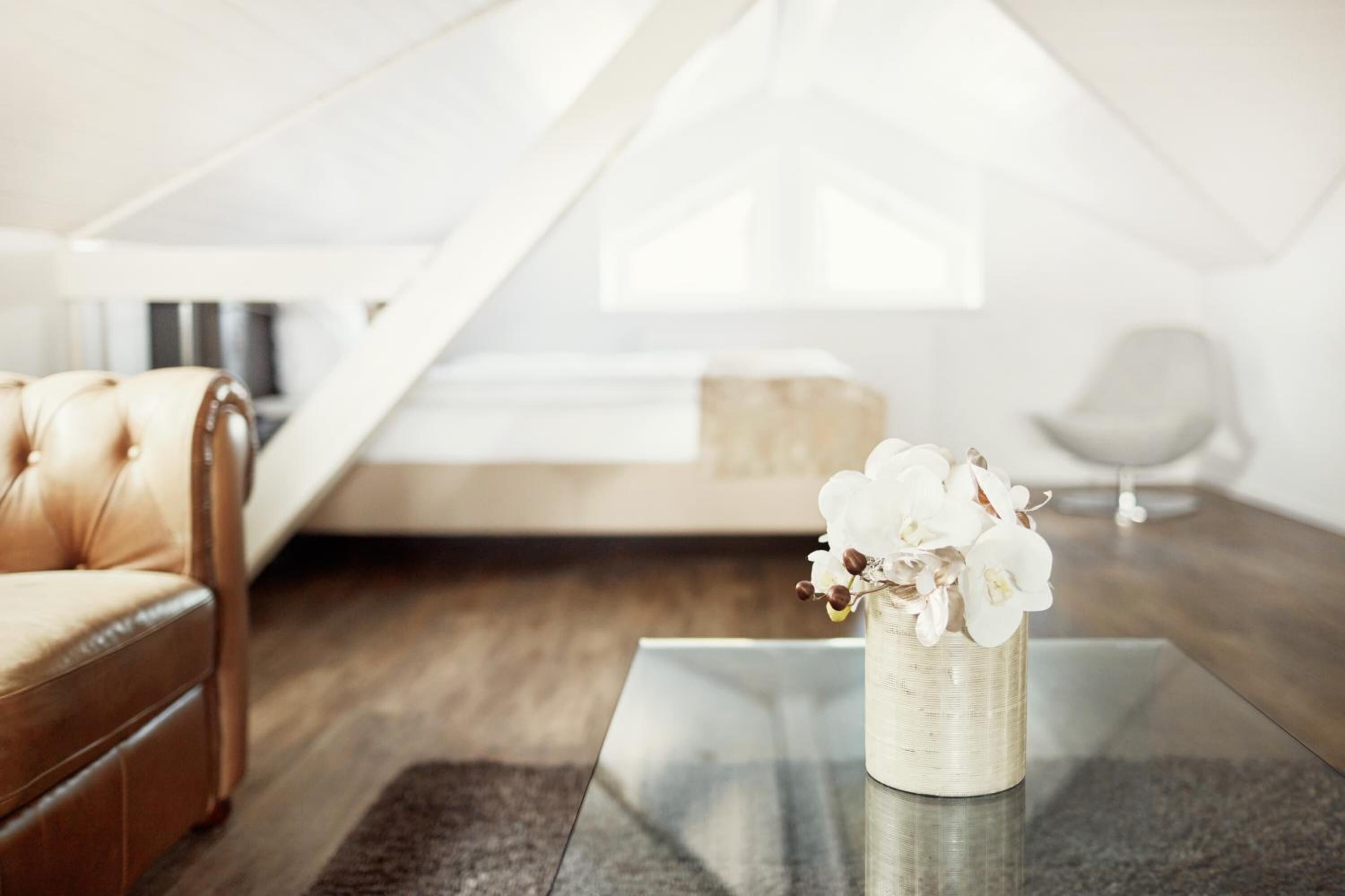A modern living room with a leather sofa, a glass coffee table, and a vase of white flowers.