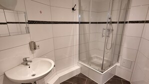 A modern bathroom with a glass-enclosed shower, a white sink, and a tiled floor. - Pension Puschkin Berlin (Berlin)