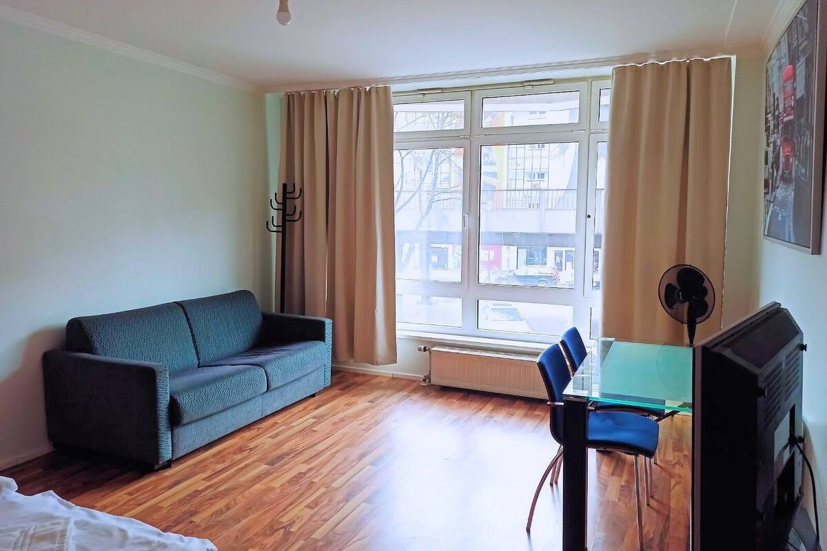 A room with a sofa, a chair, a table, a TV, and a window with curtains.