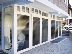 A modern building with large glass doors and windows, a white exterior, and a paved entrance area. - Garnì Seventy Design Rooms (Dimaro Folgarida)