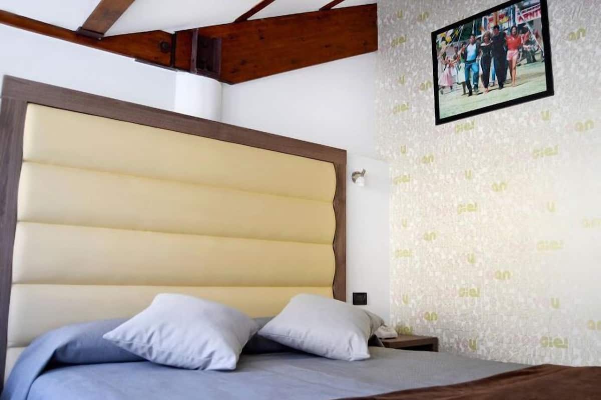 A bedroom with a large bed, wooden beams, a patterned wallpaper, and a framed photo on the wall.