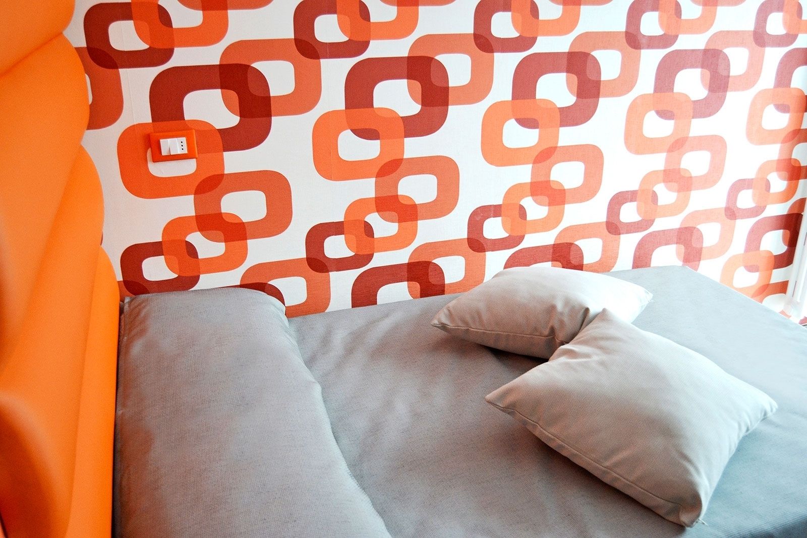 Un letto con cuscini grigi e una testata arancione davanti a una parete decorata.
