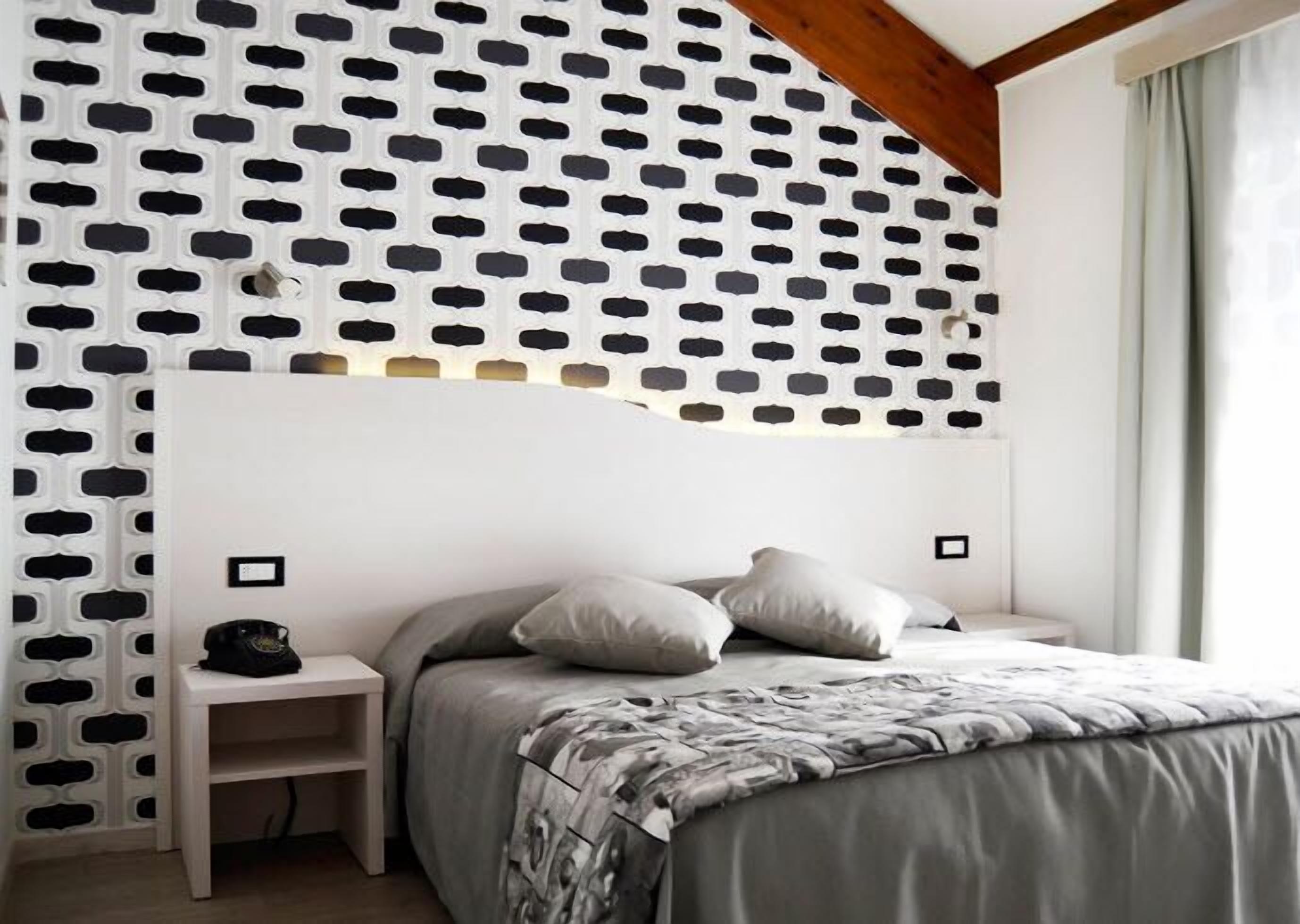 Ein Schlafzimmer mit weißem Kopfteil, einem Bett mit grauer Decke, zwei Nachttischen und einer Wand mit Muster.