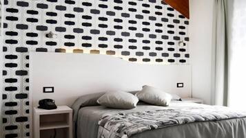 Ein Schlafzimmer mit weißem Kopfteil, einem Bett mit grauer Decke, zwei Nachttischen und einer Wand mit Muster.