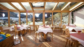 A dining area with wooden tables and chairs, large windows with mountain views, and a wooden ceiling structure. - Natur Residenz Blaslerhof (Valle di Casies)