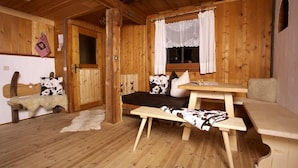 A rustic wooden cabin interior with a bed, a bench, a table, and a window with curtains. - Natur Residenz Blaslerhof (Valle di Casies)