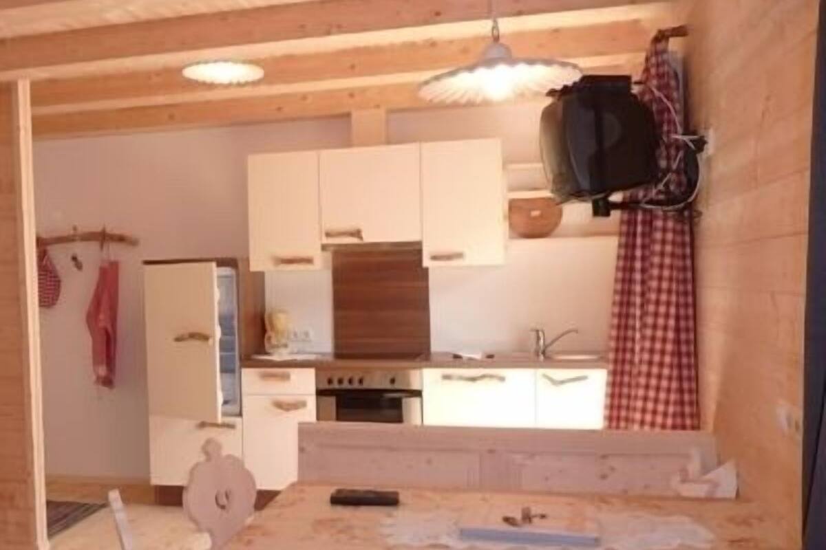 Una cocina con armarios blancos, encimera de madera y una lámpara colgante.