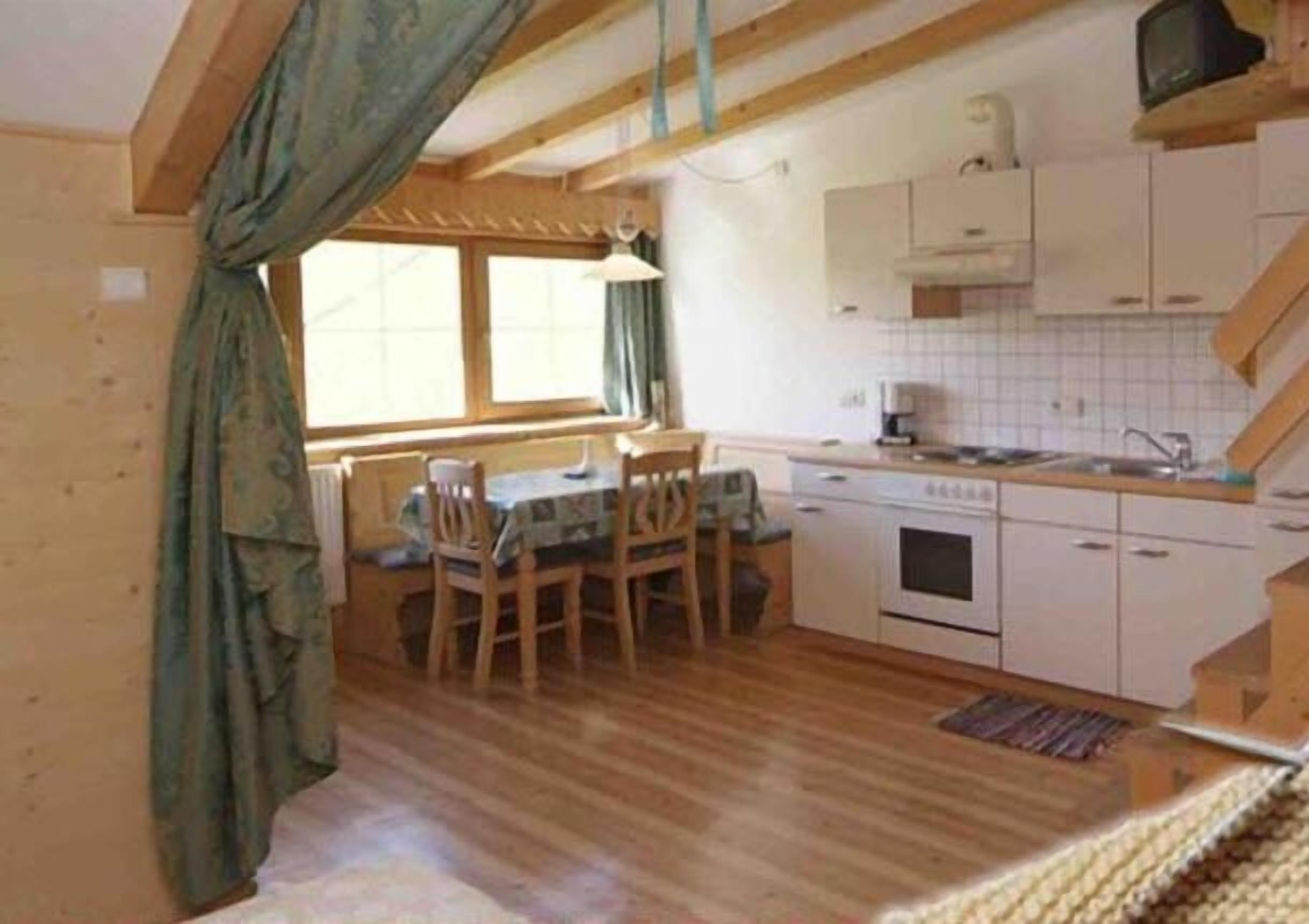 Eine kleine Küche mit Holzschränken, einem Esstisch und einem fenster mit Vorhängen.