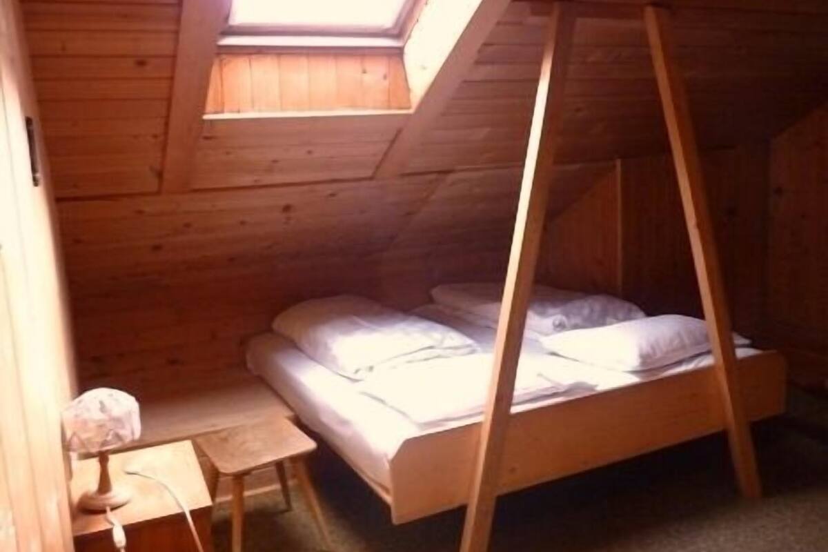 Un dormitorio pequeño de madera estilo ático con una cama individual, una mesita y un tragaluz.