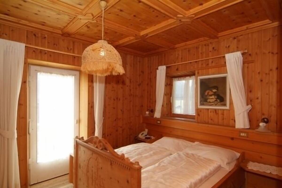 Habitación de cabaña de madera con cama, lámpara colgante, ventana con cortinas y un cuadro en la pared.
