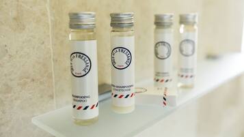 Cuatro botellas de champú y acondicionador sobre un estante blanco frente a una pared con textura.