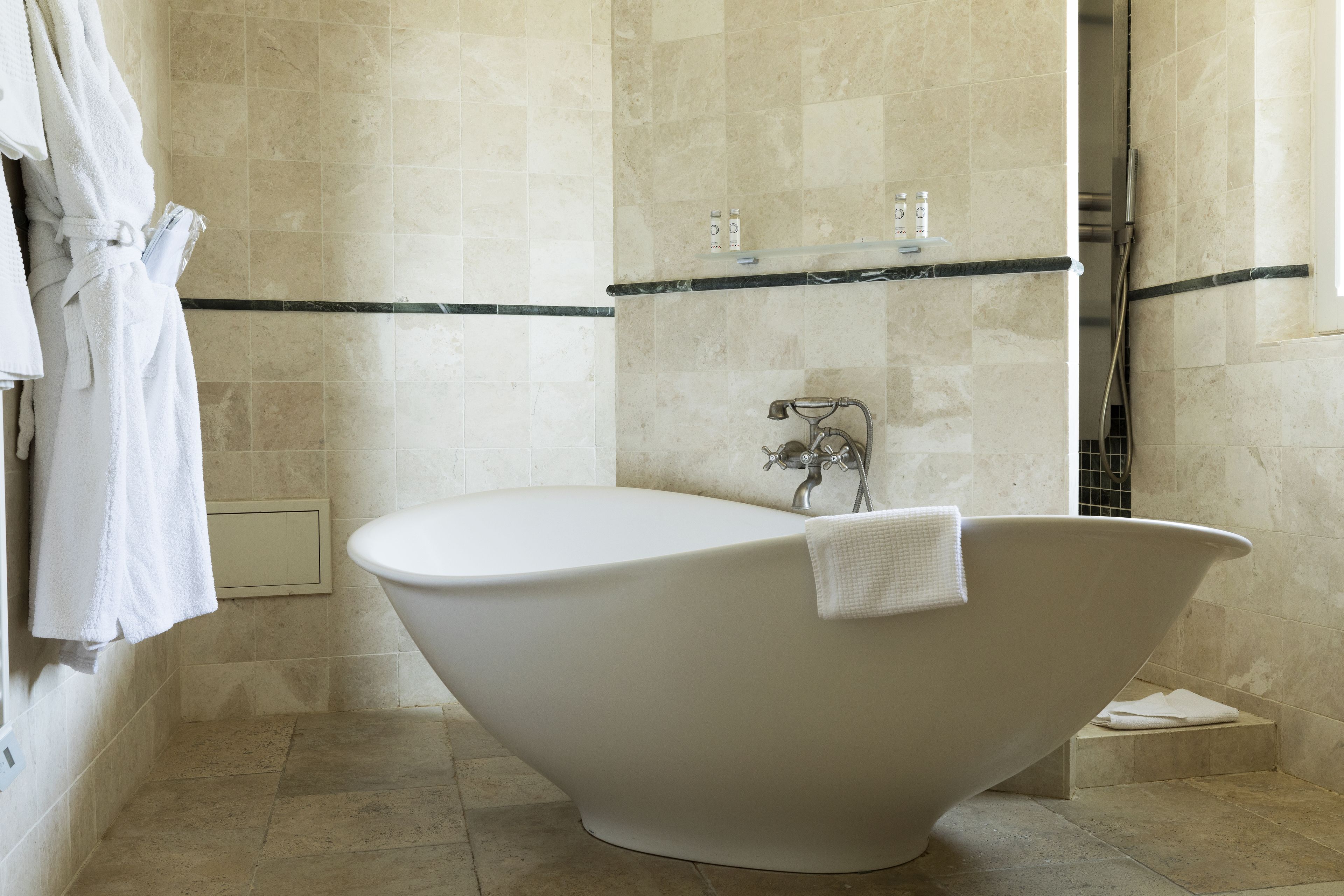 Une salle de bain moderne avec une baignoire sur pieds, une douche et une étagère en verre où sont rangés les articles de toilette.
