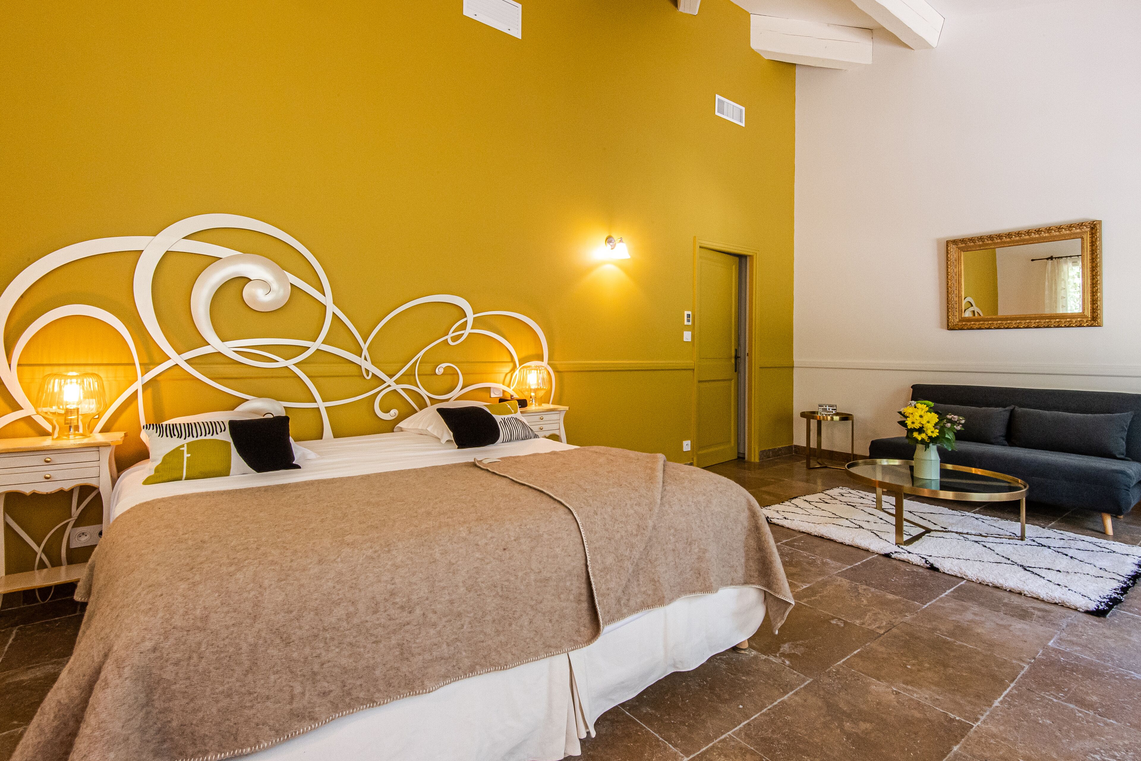 A bedroom with a bed, bedside tables, a sofa, a coffee table, and a mirror.