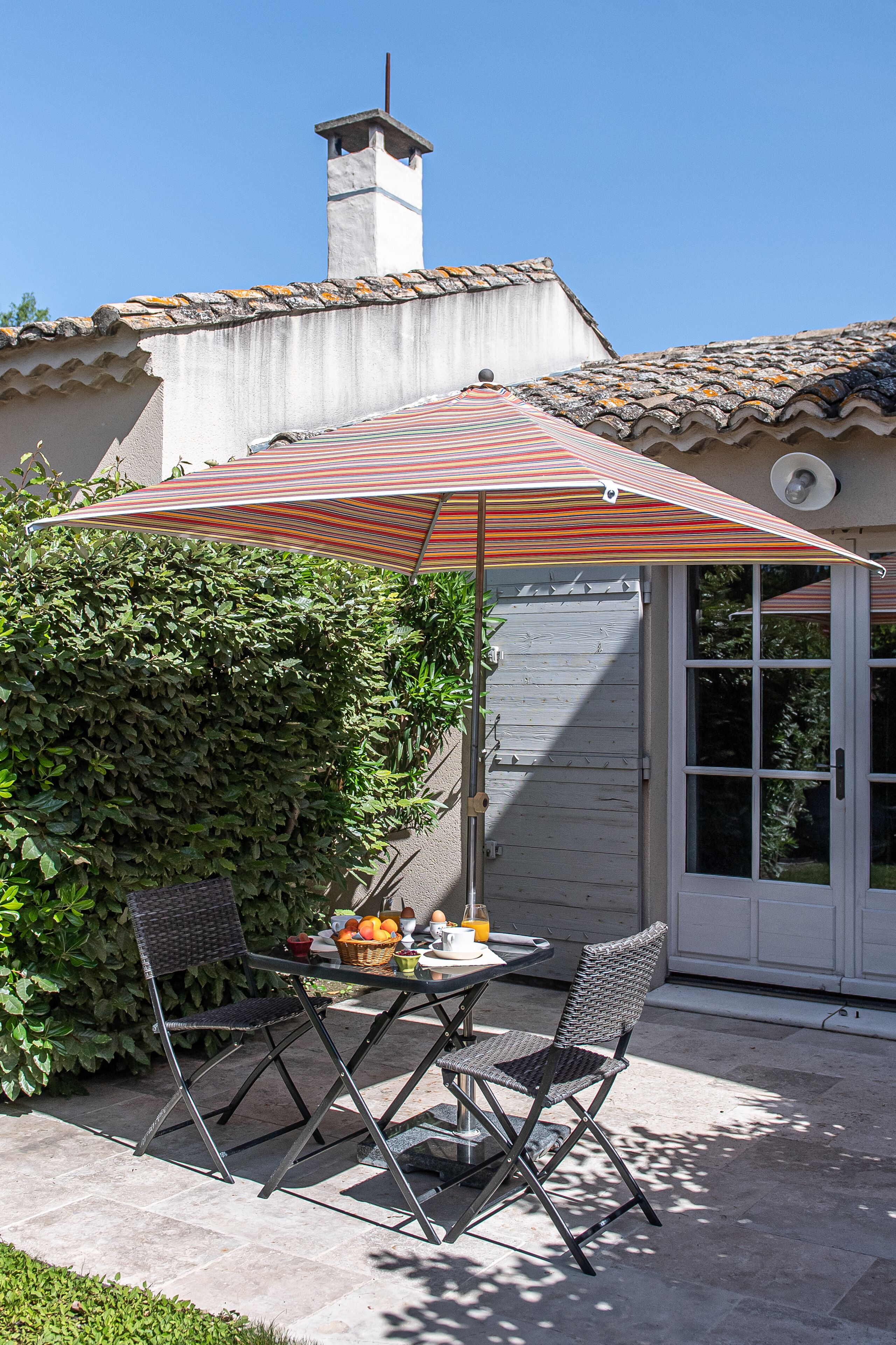 Une terrasse extérieure avec une table, deux chaises et un parasol à rayures.