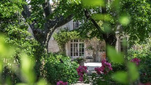Un chemin de jardin mène à un bâtiment doté d’une façade en pierre et de grandes fenêtres.