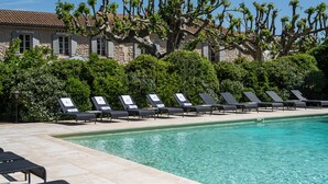 Un espace aménagé au bord de la piscine, avec des chaises longues et un bâtiment en pierre surmonté d’un toit en tuiles.