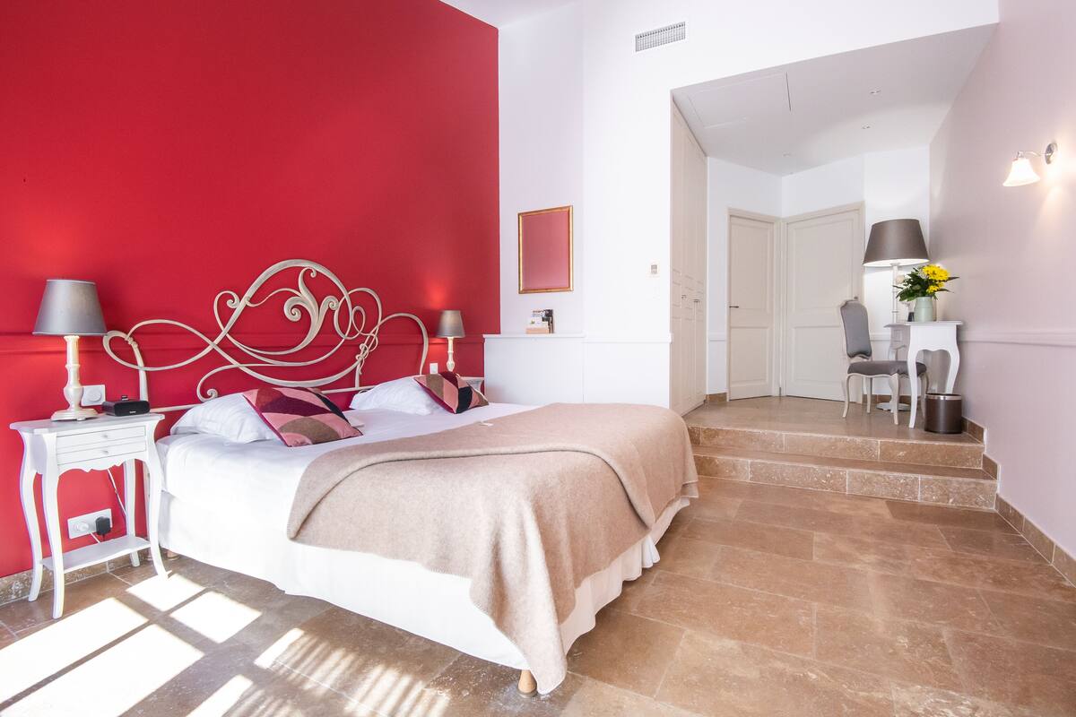 Une chambre avec un mur d’accent rouge, un lit blanc et un escalier menant à une salle de bain.